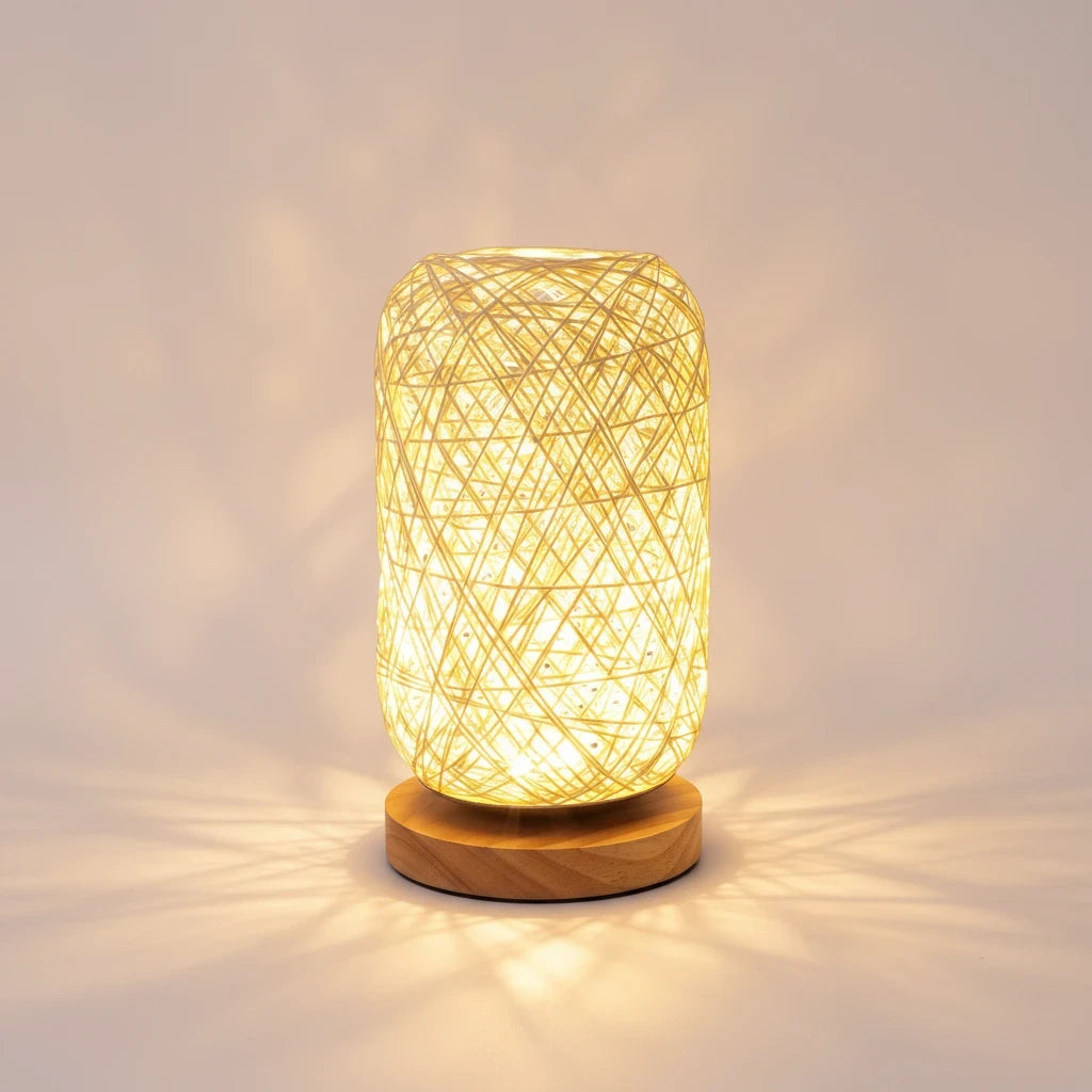 woodnestcraft handwoven rattan table lamp with a natural wood base emitting a warm glow on a neutral background