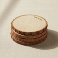 woodnestcraft set of four round natural wood slice coasters with rustic bark edges on a textured beige fabric surface
