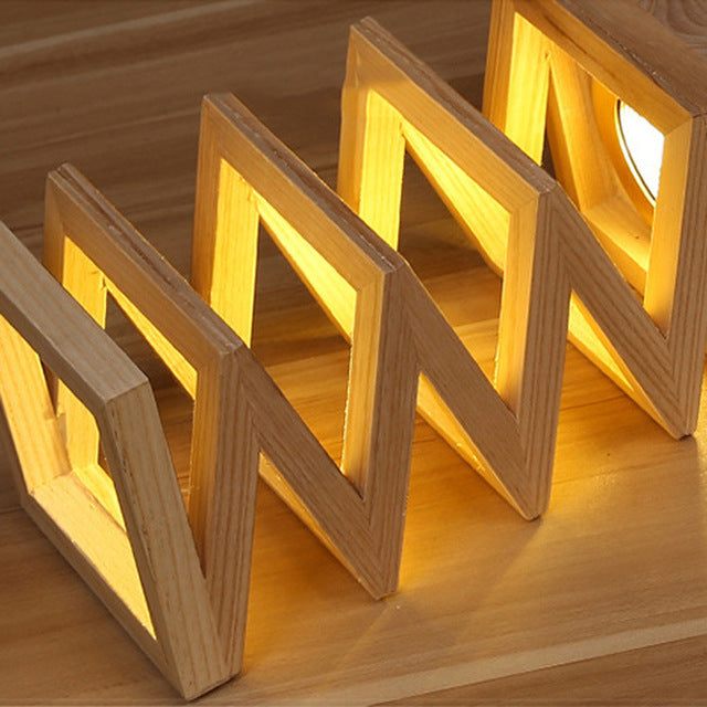 woodnestcraft accordion lamp made of solid wood panels with warm glowing light on a wooden surface