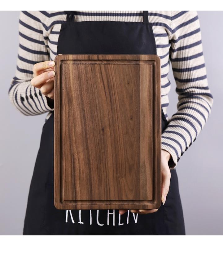 woodnestcraft rectangular solid black walnut wood cutting board with juice groove held by a person in an apron